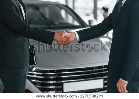 Close up view. Two businessmen are standing in the car showroom and making a deal, handshake.