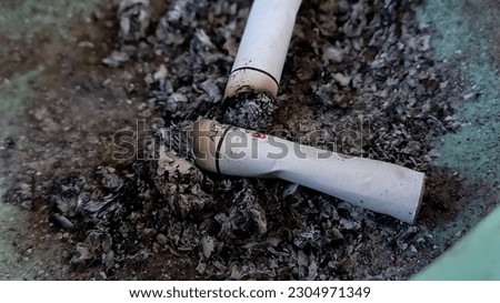 Close up view of two cigarette butts in a dirty ashtray, rarely cleaned and filled with ashes