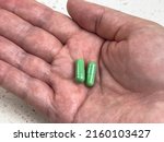 Close up view of two green pills in the palm of an adult hand, shot against a light background