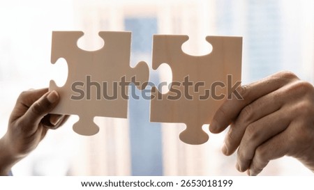 Close up view of two hands holding white pieces of jigsaw, trying to fit puzzle pieces together to overcome challenge, find solution, developing business plan or strategy. Companies merging, synergy