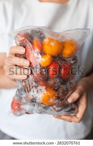 Close view of two hands presenting a sealed bag of frozen cherry tomatoes for food storage and recipe prep background.