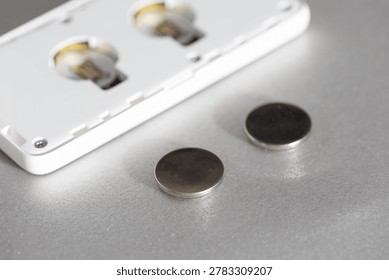 Close up view of two new round button cell batteries positioned on reflective silver surface, prepared for insertion into back of open modern electronic device, showing empty battery slots
