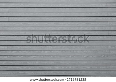 Close up view of uniform horizontal cladding panels with faux woodgrain embossing, slight overlaps forming dark linear gaps, shot in diffuse daylight with minimal composition.