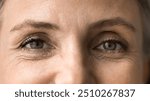 Close up view, upper face part of older pretty woman eyes, with signs of aging, advertises anti-wrinkles cream or cosmetology treatment to prevent fine lines under eyes. Wisdom, midlife, mature beauty