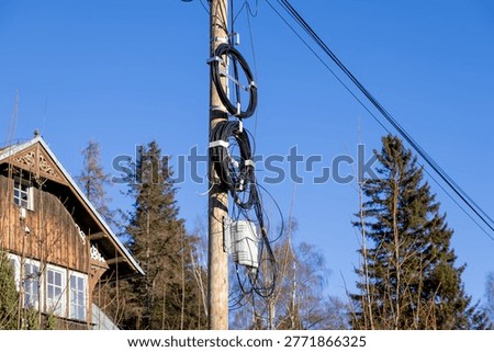 A close up view of a utility pole featuring tangled black cable loops and a grey junction box for high speed internet connectivity, representing modern digital infrastructure and rural development