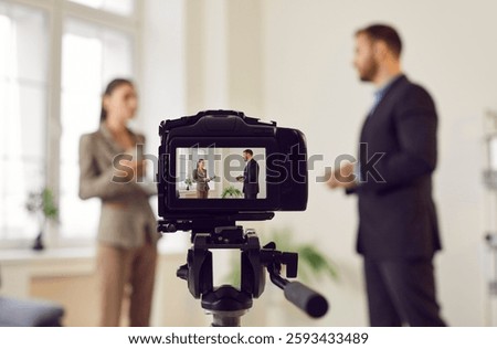 Close up view of a video camera recording an interview or hosting a live broadcast. The scene captures the interaction between a reporter and a guest, part of a TV show, news program or PR company.
