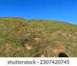 Close up view of walking path on the hill with green grass and clear blue sky on the background