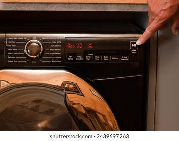 close up view of a washing machine set to low temperature wash cyle to reduce cost and energy to clean laundry, persons hand shown about to press the start button
