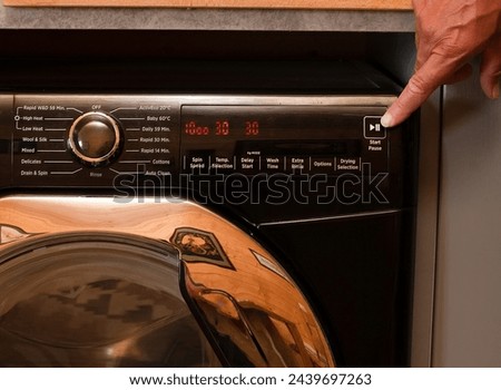 close up view of a washing machine set to low temperature wash cyle to reduce cost and energy to clean laundry, persons hand shown about to press the start button