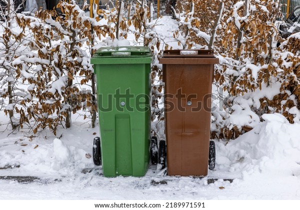 Close up view of waste and recycling\
containers on snowy bushes background. Sweden.\
