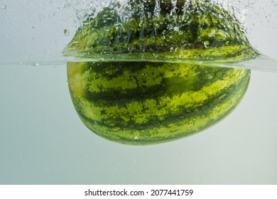 Close up view of watermelon falling into water on turquoise background. Gorgeous backgrounds. 