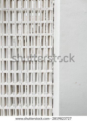 Close up view of a white rectangular breeze block roster wall connected to a smooth painted wall.