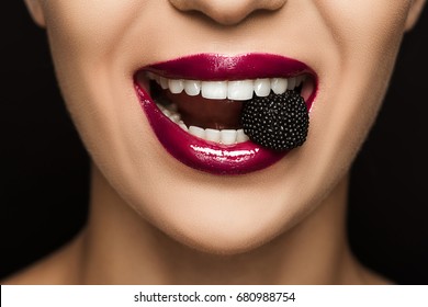 close up view of woman with black jelly candy in mouth, isolated on black   