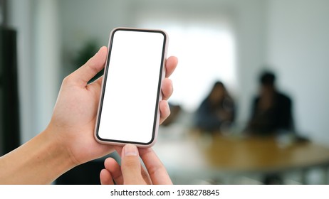 Close up view of woman holding mobile phone with blurred office room background.