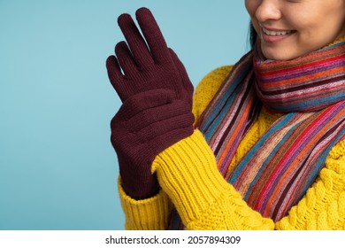 Close up view of the woman in stylish yellow sweater putting on her gloves. Cool girl in warm knitted scarf and gloves posing on blue background. Winter concept