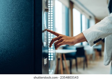 Close up view of woman's finger pushing number button on keyboard of snack vending machine. Self-used technology and consumption concept