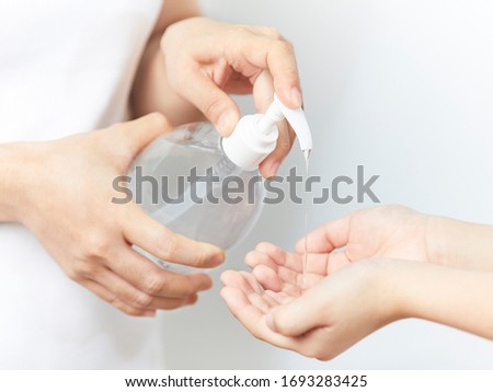 Close up view of women wearing white shirt using small portable alcohol gel, sanitizer hand gel bottles for killing bacteria, virus, germs on kid 's hand.