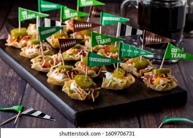 A close up view of a wooden platter of layered dip appetizers topped with jalapenos ready for a Super Bowl party.