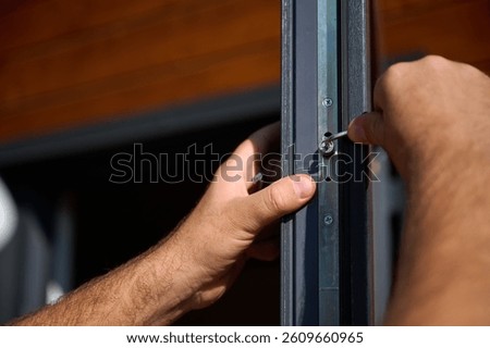 Close up view of worker installing door and window in a new house construction site. Man in uniform with hex key adjusting front glass door and windows in new beautiful house. Crop view.