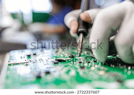 Close view of worker in protective gloves soldering electronic circuit board with hot iron during electronics assembly process
