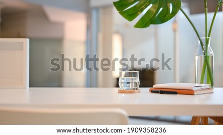 Close up view of worktable with a glass of water, copy space, stationery, decorations and plant vase in living room