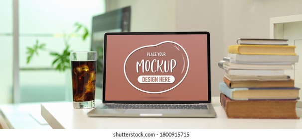 Close up view of worktable with mock up laptop, a glass of beverage and stack of  books in home office room