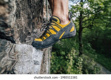 Close up view of a yellow climbing shoe on the rock. Climber's feet with orange and black climbing shoes. Rock climbing equipment in use.