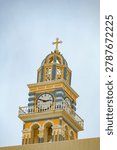 Close view of the yellow clock tower of the Catholic Cathedral of Saint John the Baptist in Fira under cloudy sky.
