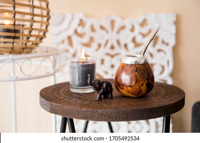 Close up view of yerba mate tea calabash with metal bombilla straw and elephant figurine on small table in modern living room, sofa couch background with oriental details. - Powered by Shutterstock