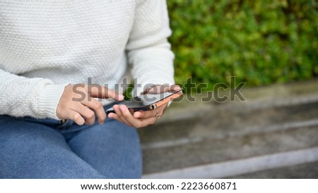 Close up view of young female using smartphone in the park while sitting 