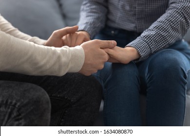 Close up view young loving couple seated together on couch holding hands, gesture symbol of care and sincere feelings, declaration of love and marriage proposal, support protection of soulmate concept