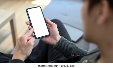 Close Up View Of Young Man Holding Mobile Phone With Empty Screen While Sitting On Sofa At Home.