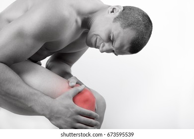 Close up view of a young man holding his knee in pain, isolated on white background. Knee and leg pain. Young man touching his knee for the pain. Red inflammation effect.