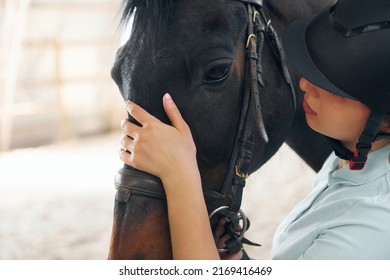 Close up view. A young woman in jockey clothes is preparing for a ride with a horse on a stable. - Shutterstock ID 2169416469