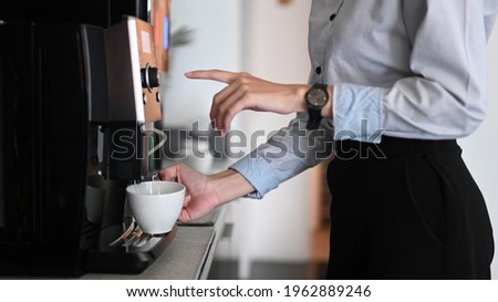 Close up view of young woman making coffee with coffee machine during office break time.