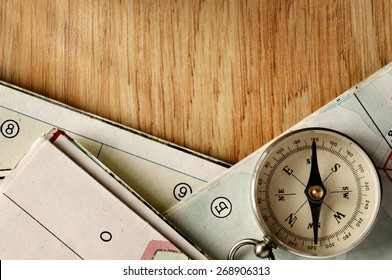 Close Up Vintage Compass Instrument On Top Of A Wooden Table With Folded Maps, Captured In High Angle View.