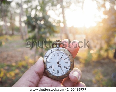 Close up of vintage pocket watch in woman hand with forest in the sunset time as background.