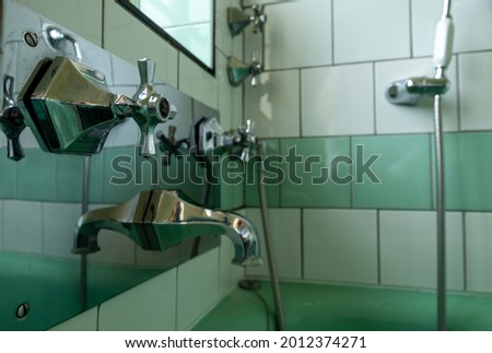 Close up of vintage retro 1930s stainless steel taps in a green and white tiled bathroom.