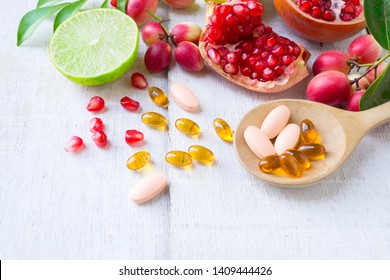 Close up vitamin supplements on wooden spoon with healthy fruits berry, lime, pomegranete on white wooden background.