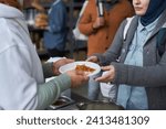 Close up of volunteer giving free hot meals to refugees at soup kitchen, focus on hands holding plate