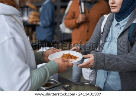 Close up of volunteer giving free hot meals to refugees at soup kitchen, focus on hands holding plate