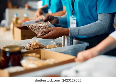 Close up of volunteer packing donated food into cardboard boxes at community center. - Powered by Shutterstock