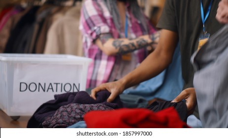 Close Up Of Volunteers Sorting Donated Clothes In Charity Shop. Team Of Workers Unpacking Boxes With Clothes In Second Hand Store. Charity And Donation Concept