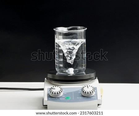 Close up of vortex liquid in beaker laboratory flask on magnetic stirrer or mixer machine for science