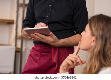 Close up of waiter hand noting down menu on tablet. Young woman ordering for food to a waiter at restaurant. Young beautiful woman thinking of food to order in front of a waiter holding tablet.  - Powered by Shutterstock