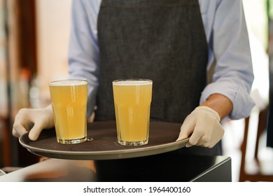 Close up waiter hand with protection gloves bringing two glasses of beer drink to serve customer as part time job
