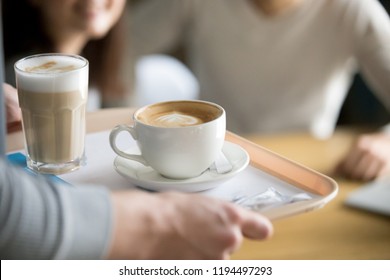 Close up of waiter holding aromatic cappuccino and latte on tray bringing order to café guests, coffeeshop worker give hot drinks to visitors, cups with delicious fresh brewed coffee on platter - Powered by Shutterstock