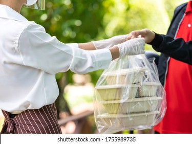 Close Up Waitress Hand Give Food Box To Deliverly Man To Deliver It To Customer Make Online Order. Food Delivery Service Concept In New Normal After Coronavirus Pandemic.  