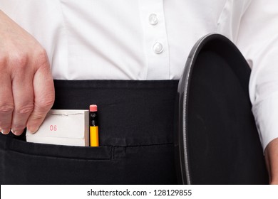 Close up of a waitress taking her order pad out of her apron pocket whilst she holds a tray in the other hand.