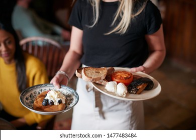 Close Up Of Waitress Working In Traditional English Pub Serving Breakfast To Guests